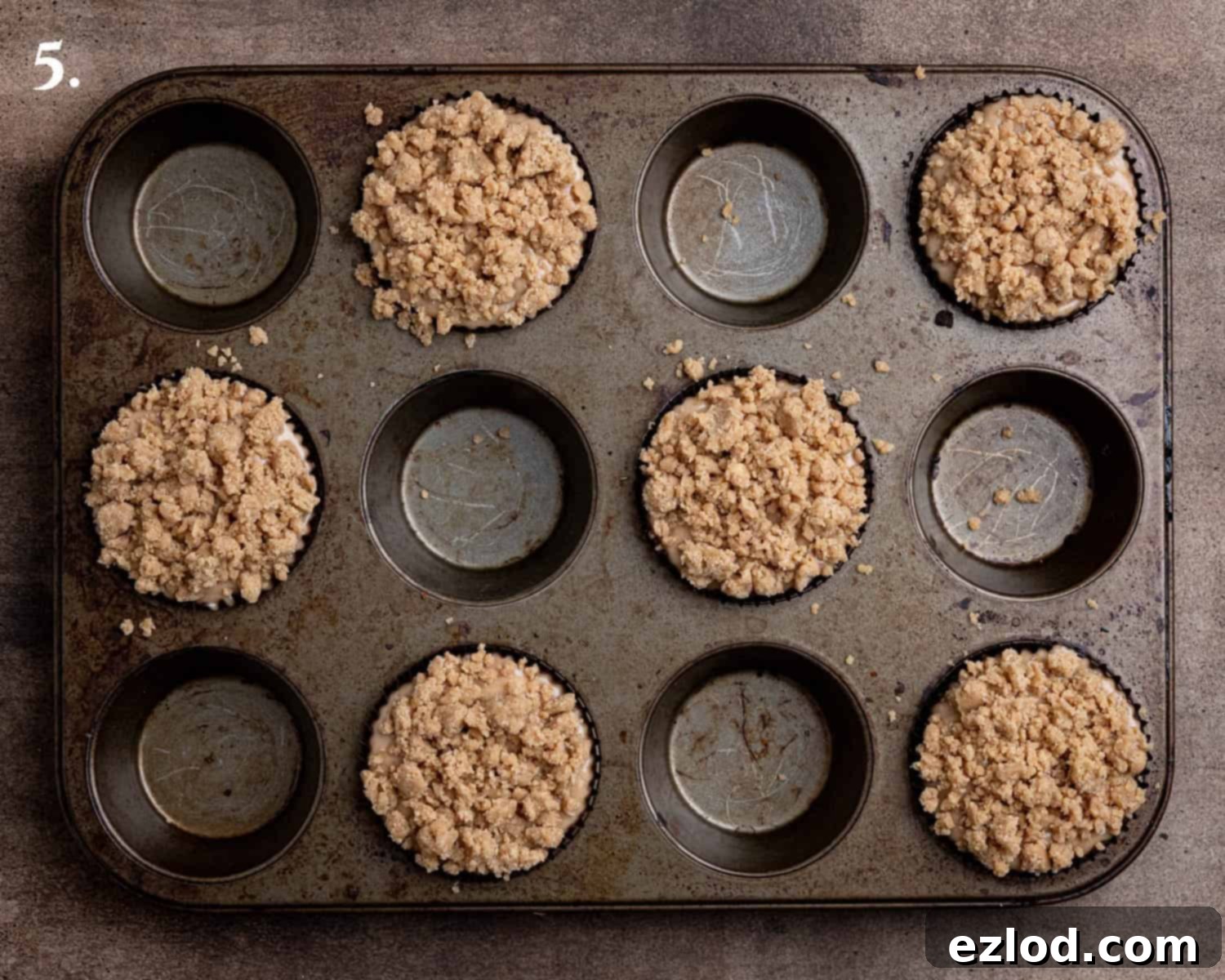 Spiced Pear Plant-Based Muffins 9 Step-by-step image of muffin cases filled with batter and topped with streusel, ready for baking.