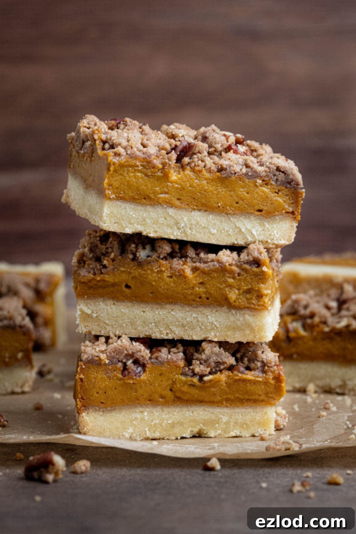 A stack of three perfectly layered vegan pumpkin crumb bars, showcasing the shortbread base, creamy pumpkin filling, and crumbly pecan streusel.