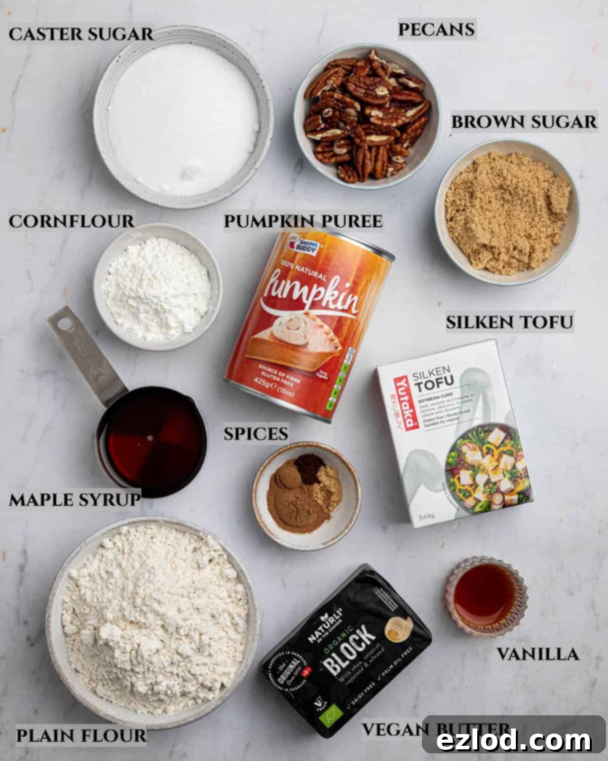 A beautifully arranged labelled photo of all the key ingredients required to bake delicious vegan pumpkin crumb bars, including pumpkin puree, spices, flours, and vegan butter.