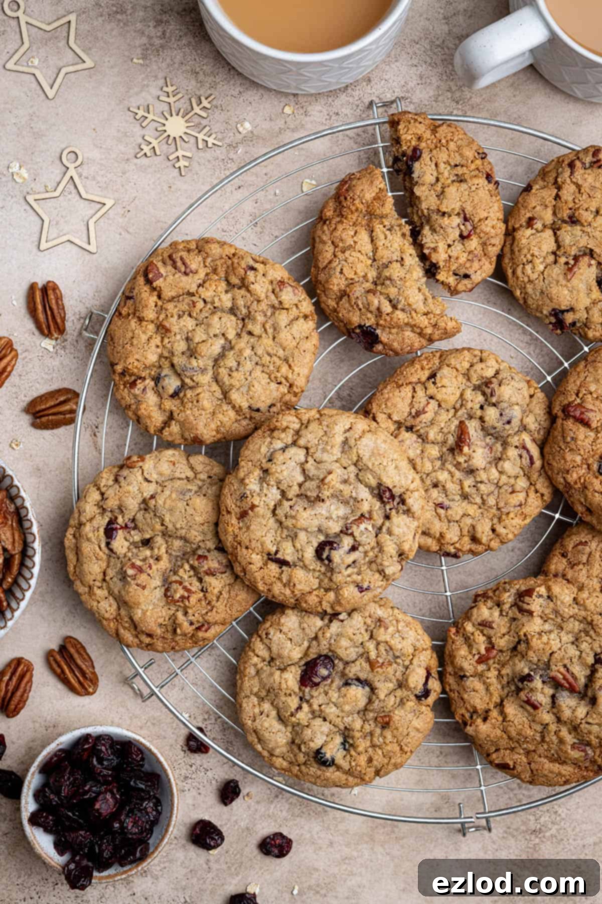 Cranberry pecan oatmeal cookies arranged on a round wire cooling rack, accompanied by cups of tea and bowls of cranberries and pecans.