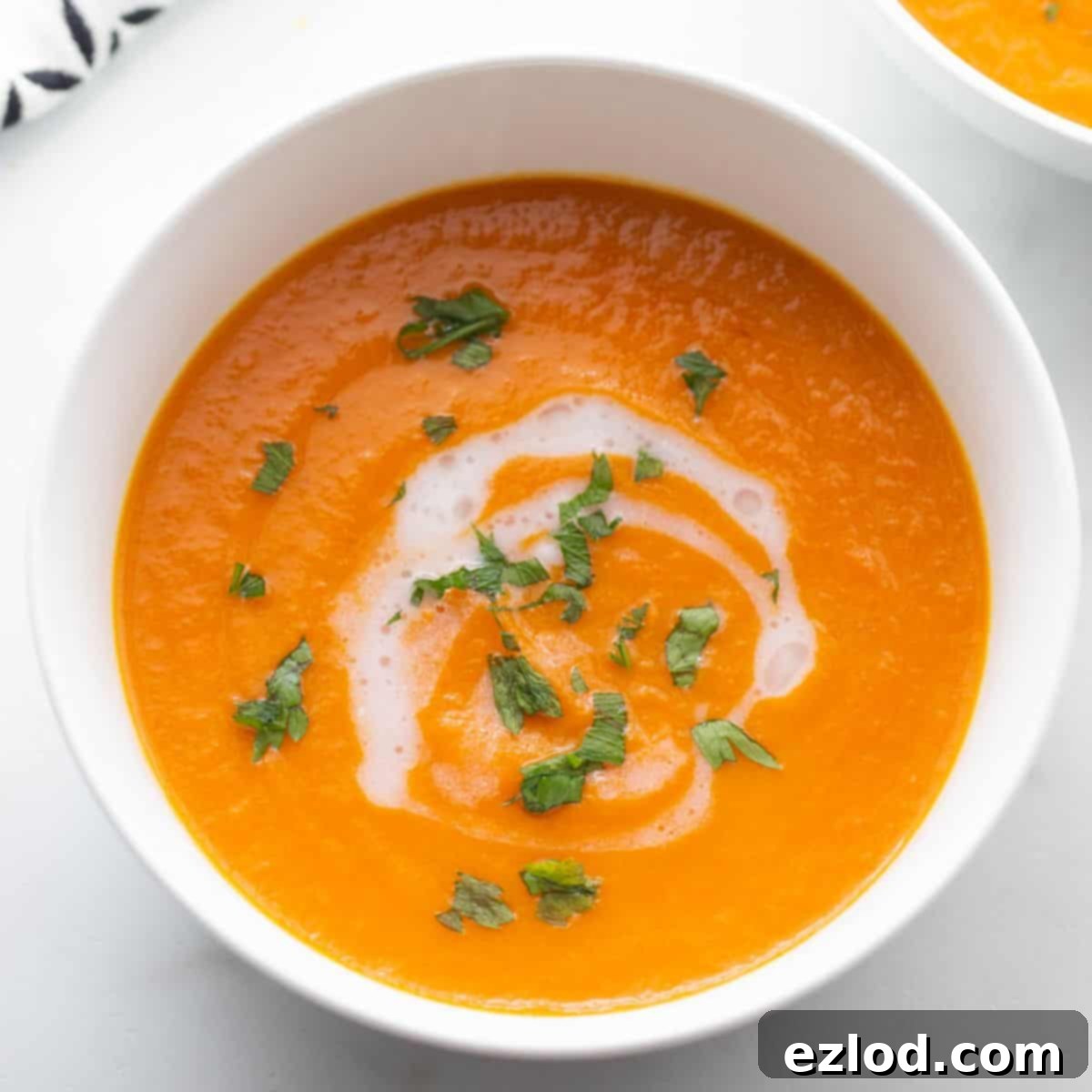 Two bowls of creamy Instant Pot carrot ginger soup with a swirl of coconut milk and a garnish of fresh parsley. 