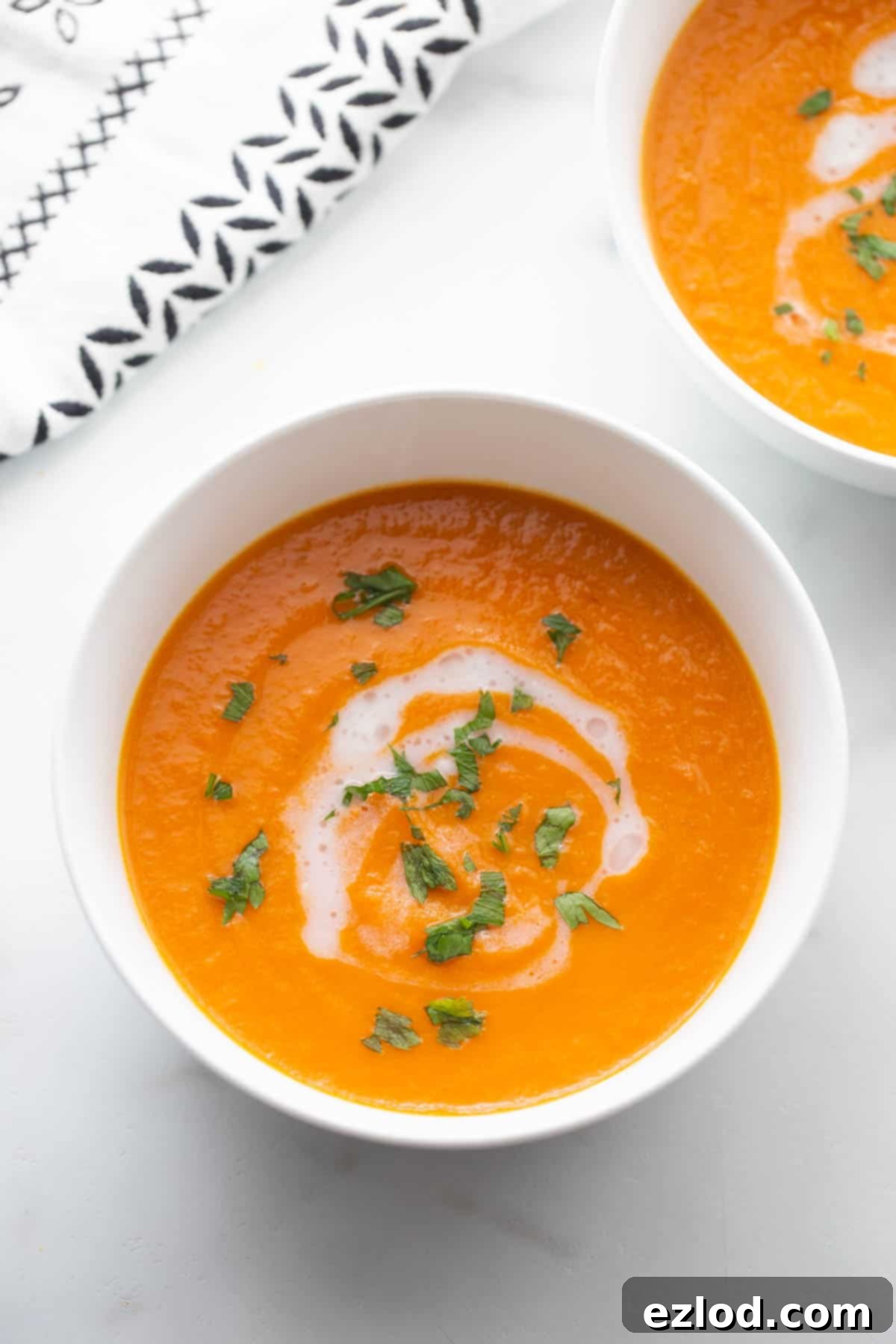 Two bowls of vibrant carrot ginger soup garnished with a drizzle of coconut milk and fresh green parsley.