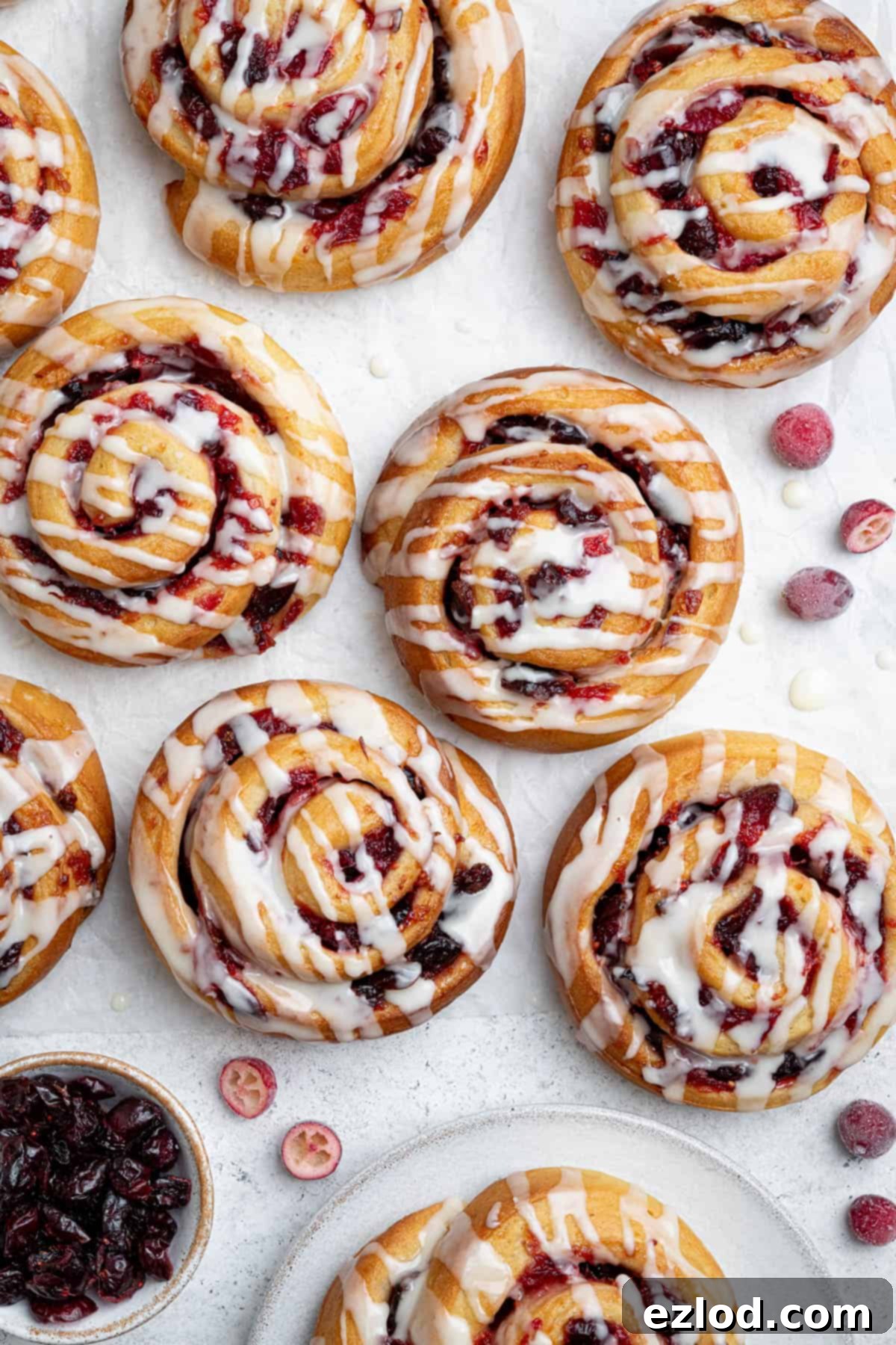 Vegan cranberry orange rolls on a white surface with fresh and dried cranberries.