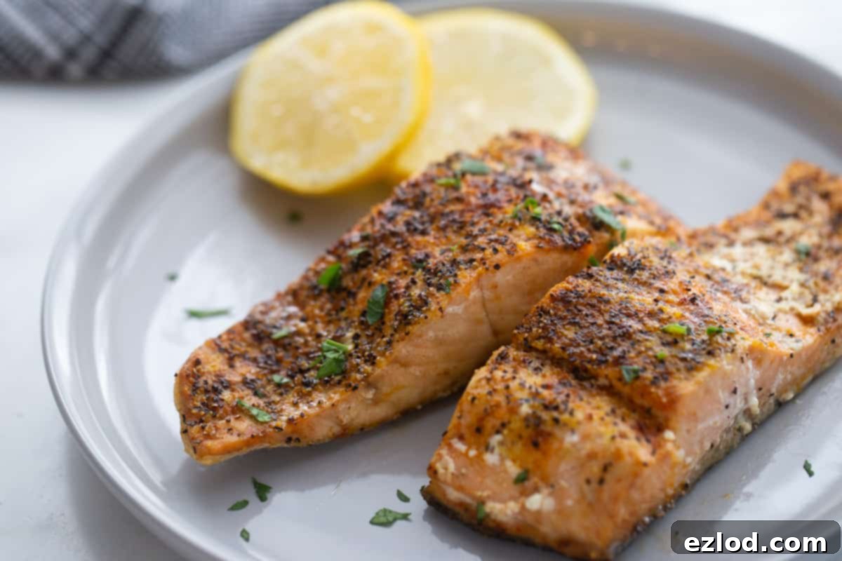 A plate with two pieces of Air Fryer Salmon cooked with seasonings and sliced lemons. 
