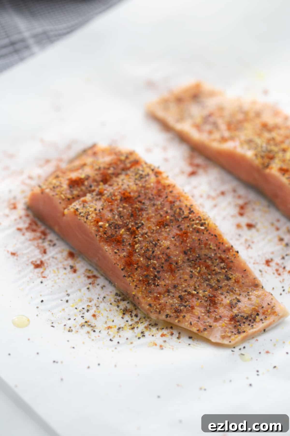 Salmon on parchment paper topped with lemon pepper seasoning. 