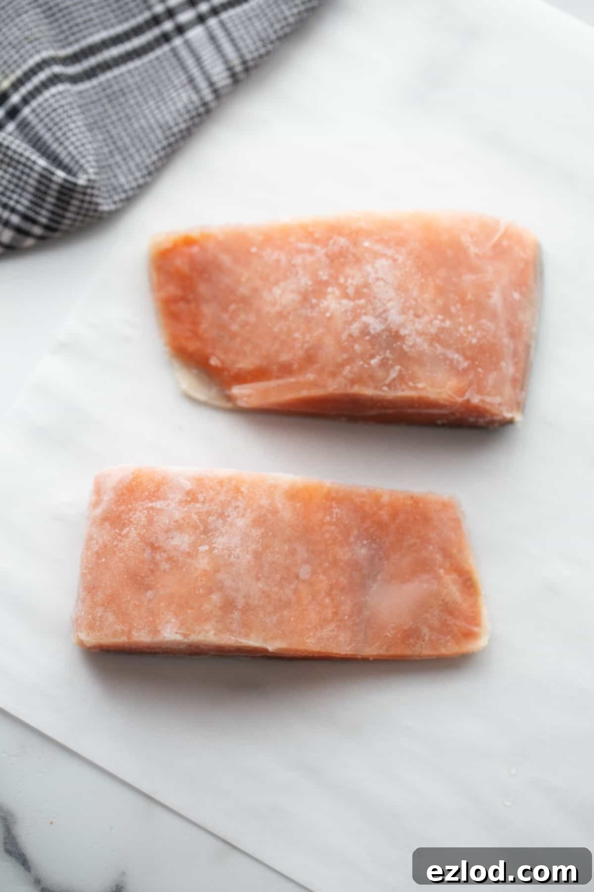 Two frozen salmon fillets on parchment paper. 