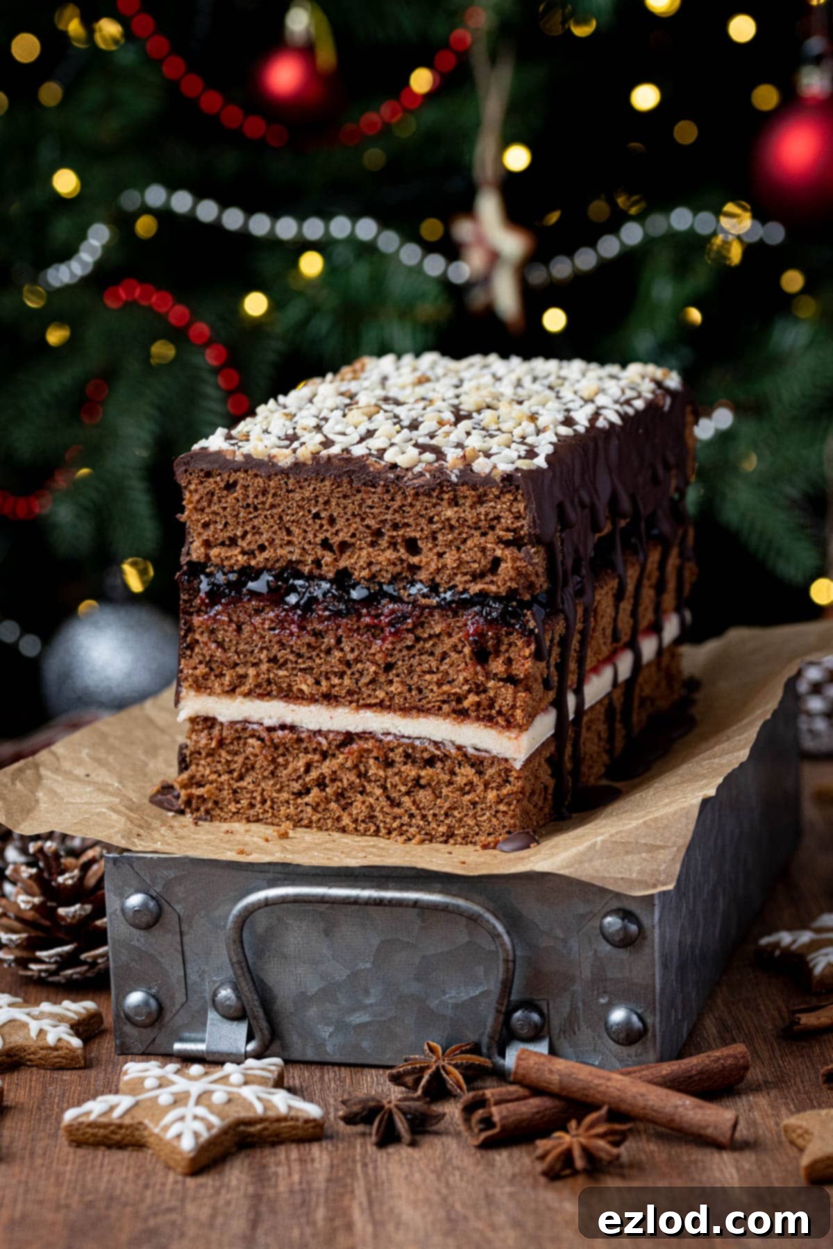 A beautifully sliced Vegan Piernik cake resting on a metal tray, with a festive Christmas tree subtly blurred in the background, showcasing its rich layers of jam and marzipan.
