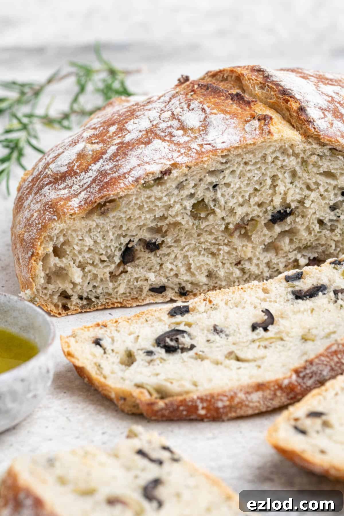 A close-up view of the perfectly golden-brown, sliced no-knead olive bread, highlighting its rustic, bubbly crust and open, airy interior with visible olive pieces.