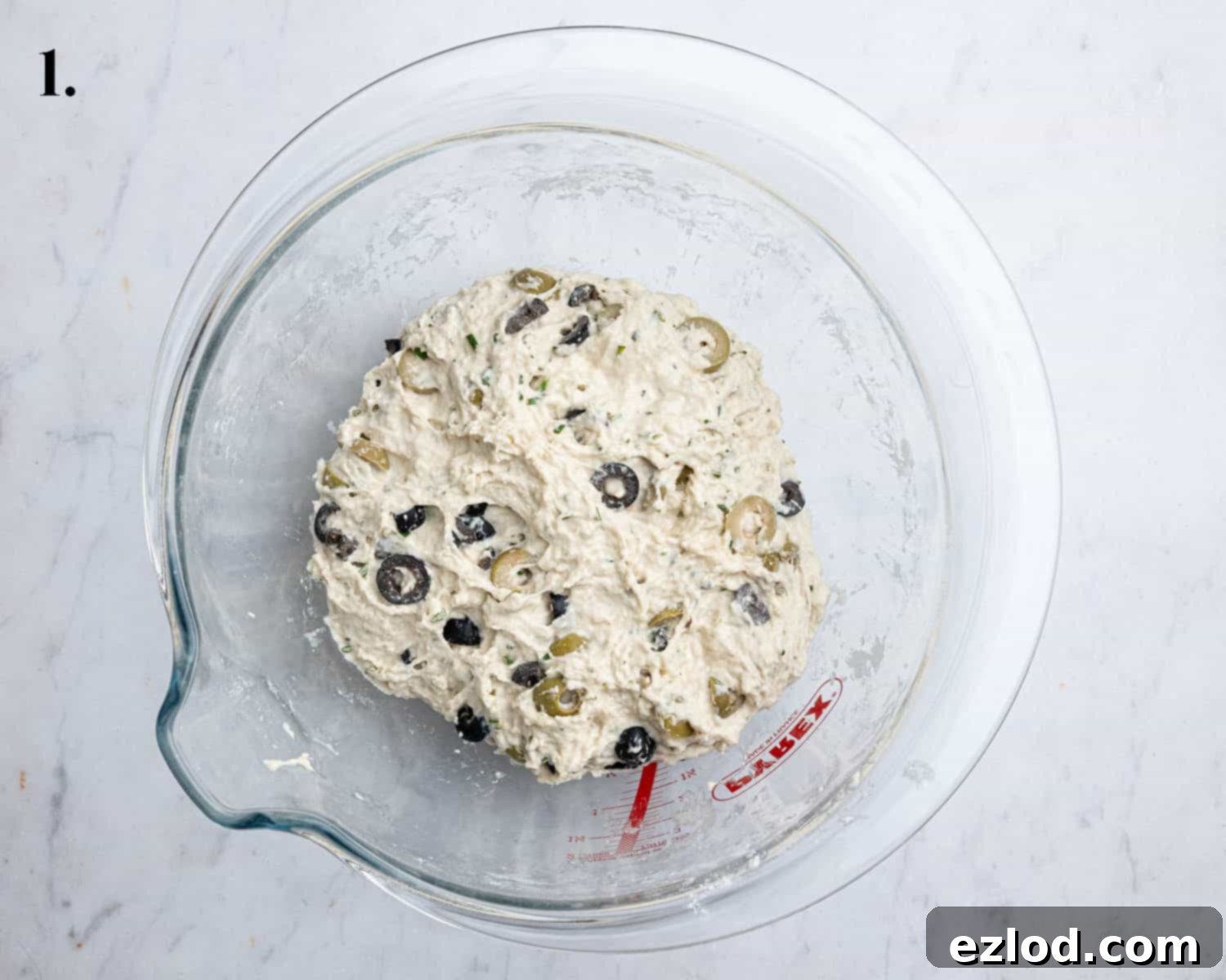 Step 1 in making no-knead olive bread: A large bowl shows the wet, sticky dough, fully mixed with flour, yeast, salt, water, olives, and rosemary, with no dry spots remaining.