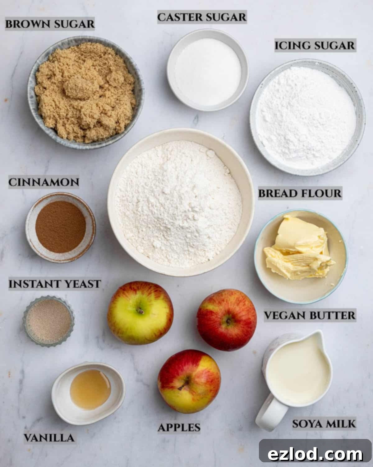 A labelled photo of the ingredients needed to make vegan apple cinnamon pull-apart bread, including bread flour, yeast, salt, sugar, non-dairy milk, vegan butter, apples, and cinnamon.