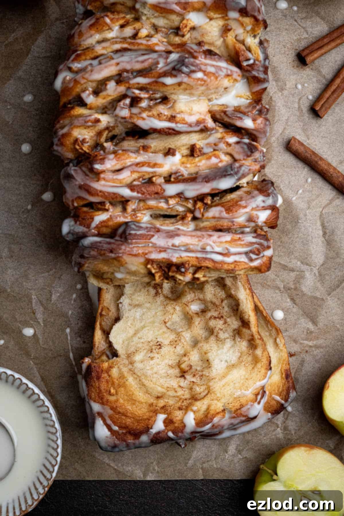 Close up of a piece of vegan apple cinnamon pull-apart bread being pulled off the main loaf, showing the soft, sticky layers and apple filling.