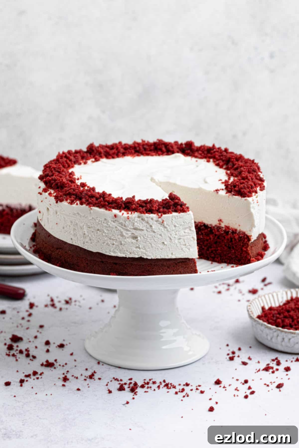Red velvet cheesecake cake with a slice removed on a white cake stand.