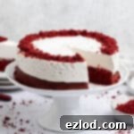 Red velvet cheesecake cake with a slice removed on a white cake stand.