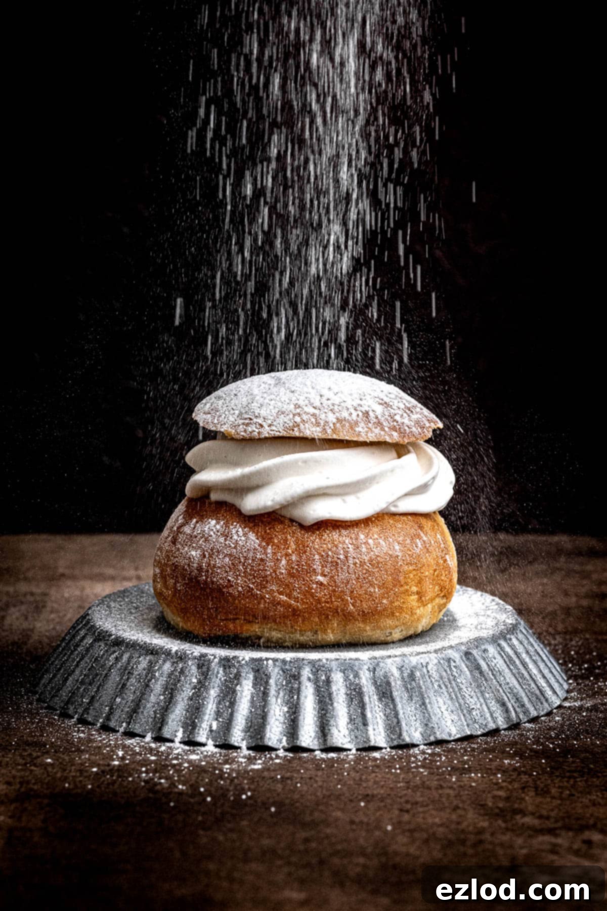 Homemade Vegan Semlor 2 A vegan semla bun on a metal plate being dusted with icing sugar.