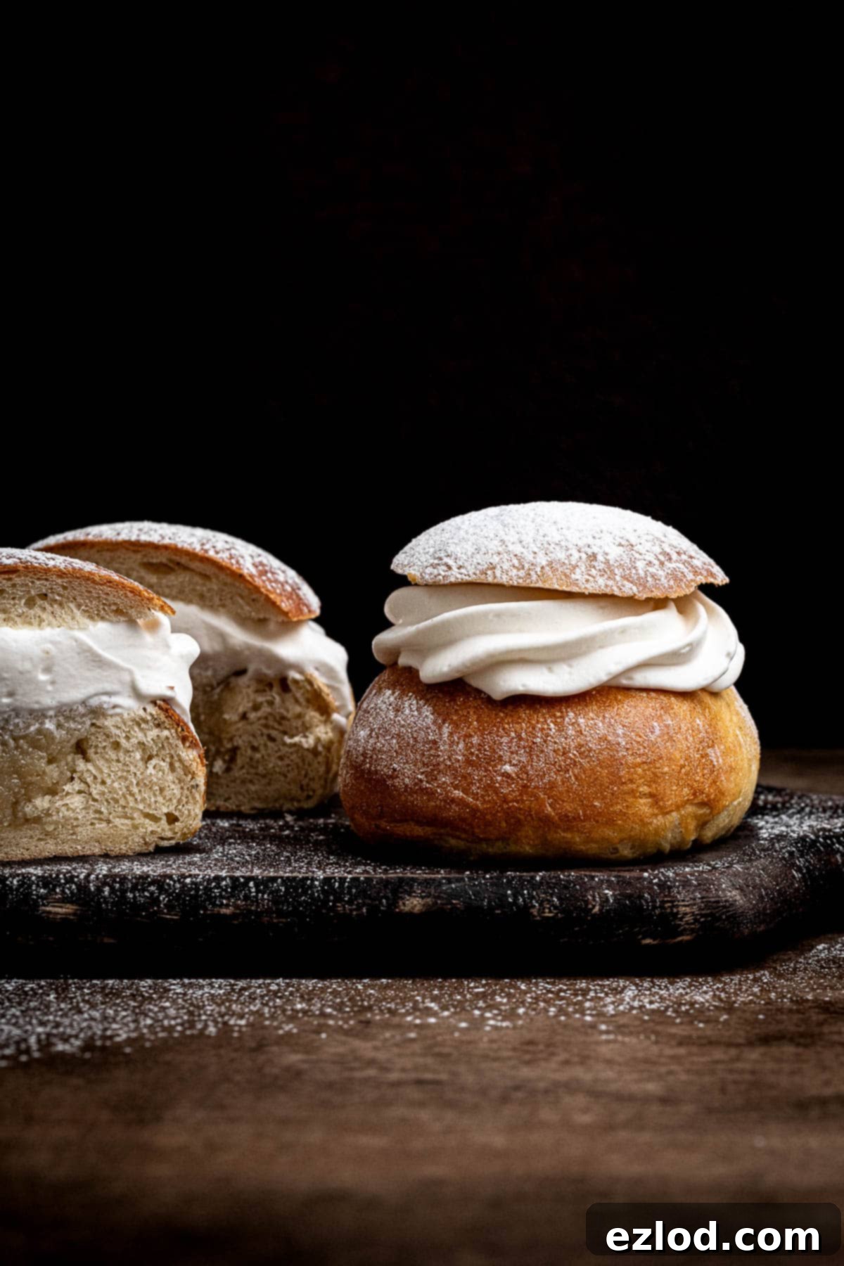 Homemade Vegan Semlor 17 Vegan semlor buns on a wooden plate, one sliced in half.