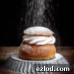 Homemade Vegan Semlor 18 A vegan semla bun on a metal plate being dusted with icing sugar.