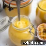 Close up of a small jar of vegan passion fruit curd with a spoon in it, ready for tasting.