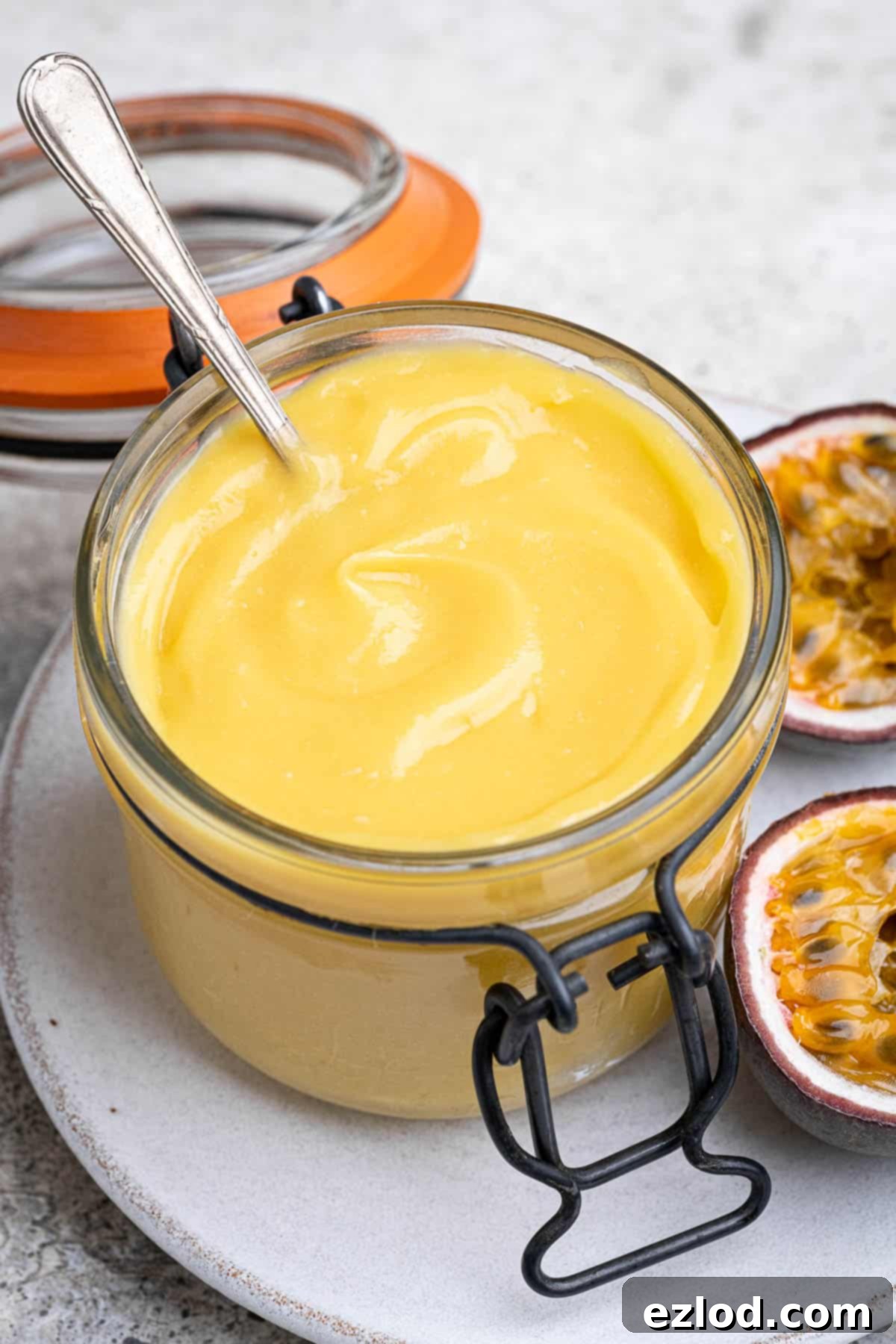 Close up of a jar of vegan passion fruit curd, showing its smooth, creamy texture and vibrant colour.
