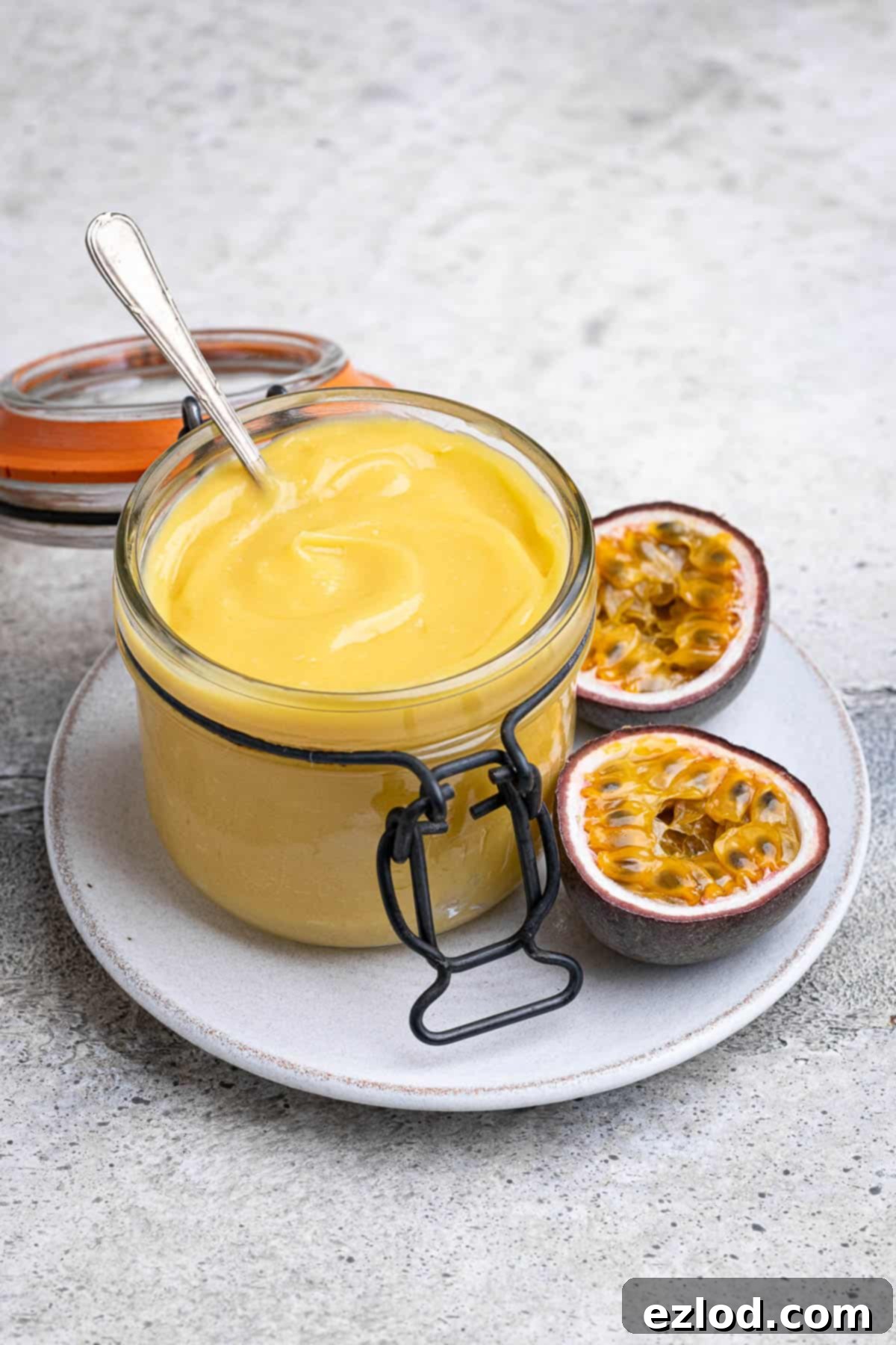 A jar of vegan passion fruit curd elegantly placed on a plate with a halved passion fruit, ready to be enjoyed.
