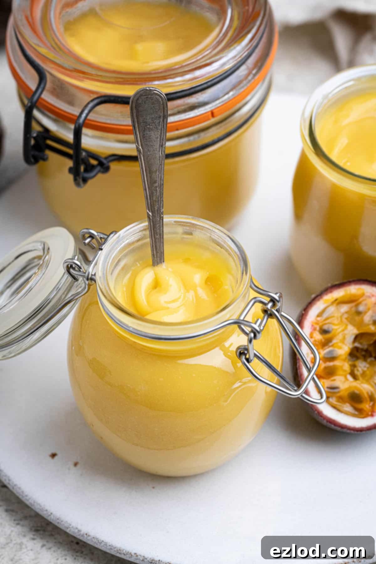 Close up of a small jar of vegan passion fruit curd with a spoon in it, inviting you to taste.