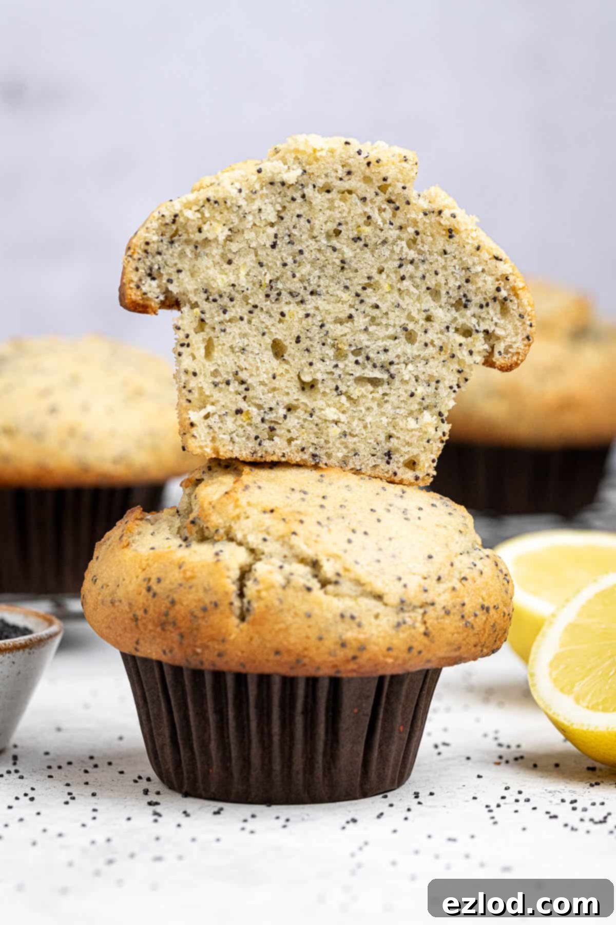 Vibrant Vegan Lemon Poppy Seed Muffins 9 A stack of delicious vegan lemon poppy seed muffins, with one perfectly cut in half to show the fluffy crumb and well-distributed poppy seeds.
