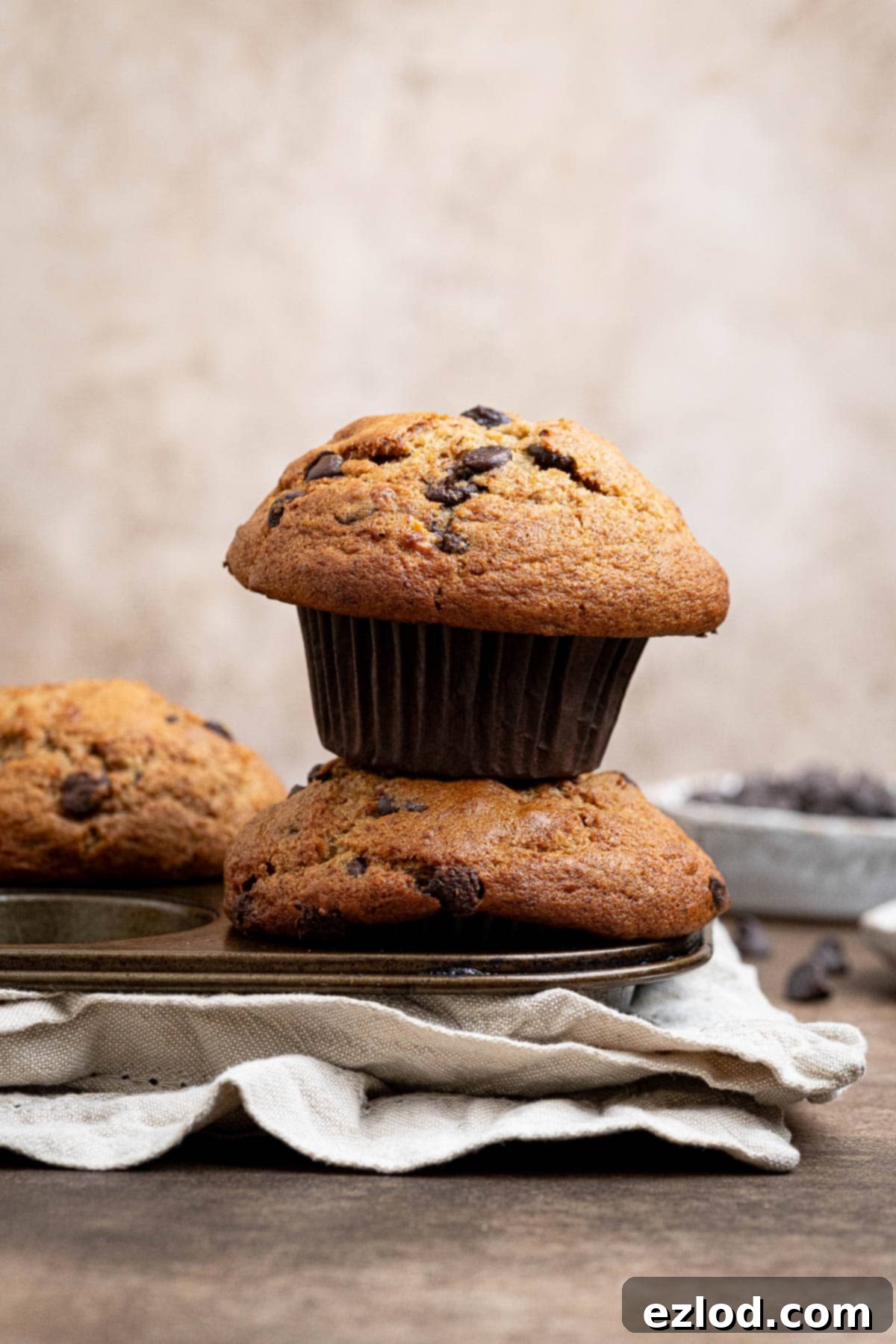 A stack of two giant, bakery-style vegan banana muffins with tall tops, on a muffin pan, showing their fluffy, moist texture.