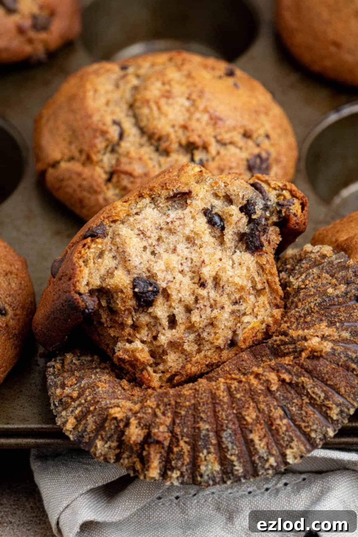 Close up of a single vegan banana muffin with a bite taken out, showcasing its moist, fluffy interior and visible chocolate chips.