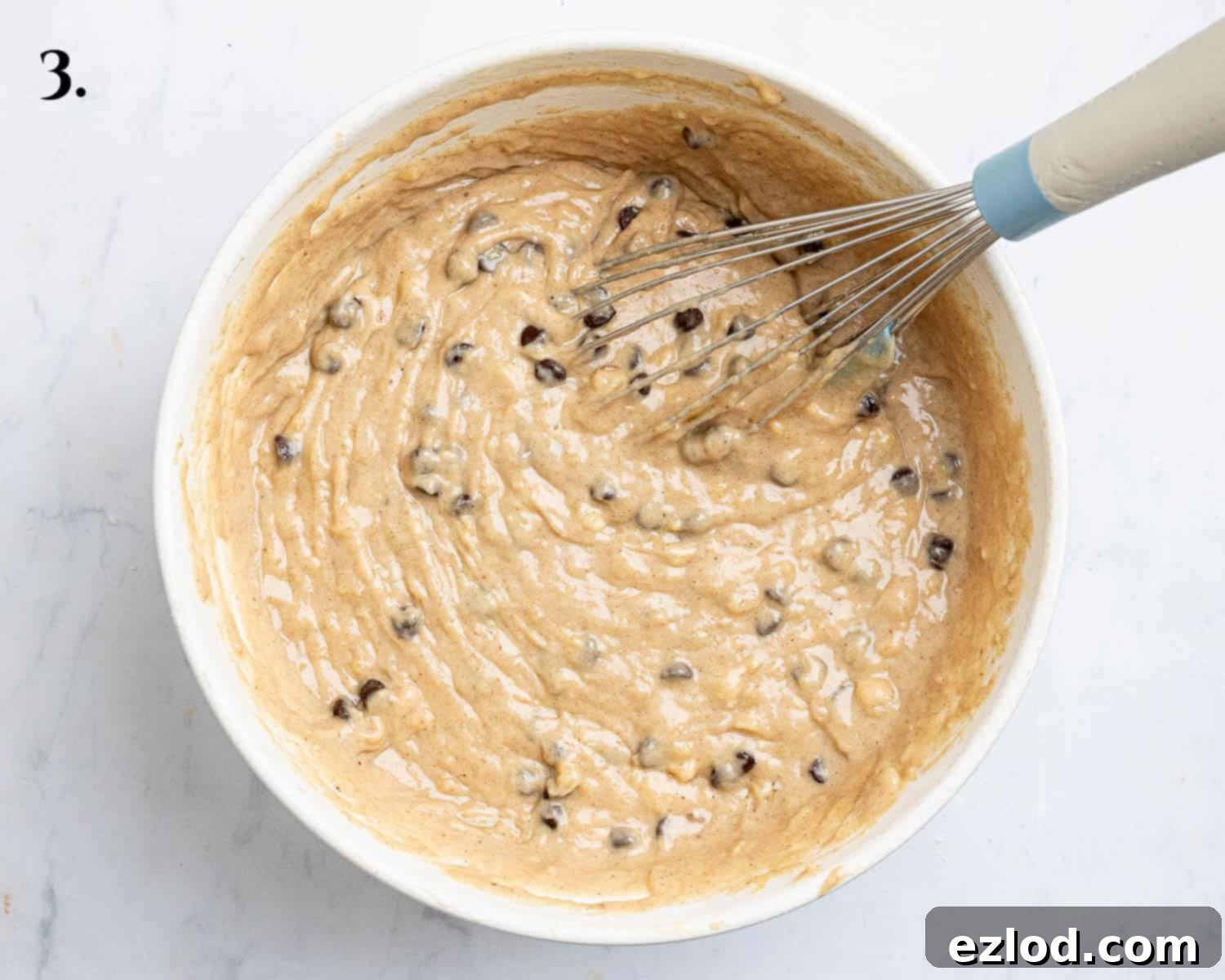 Step 3: A bowl of vegan banana muffin batter, gently mixed with flour and chocolate chips, showing a slightly thick consistency.