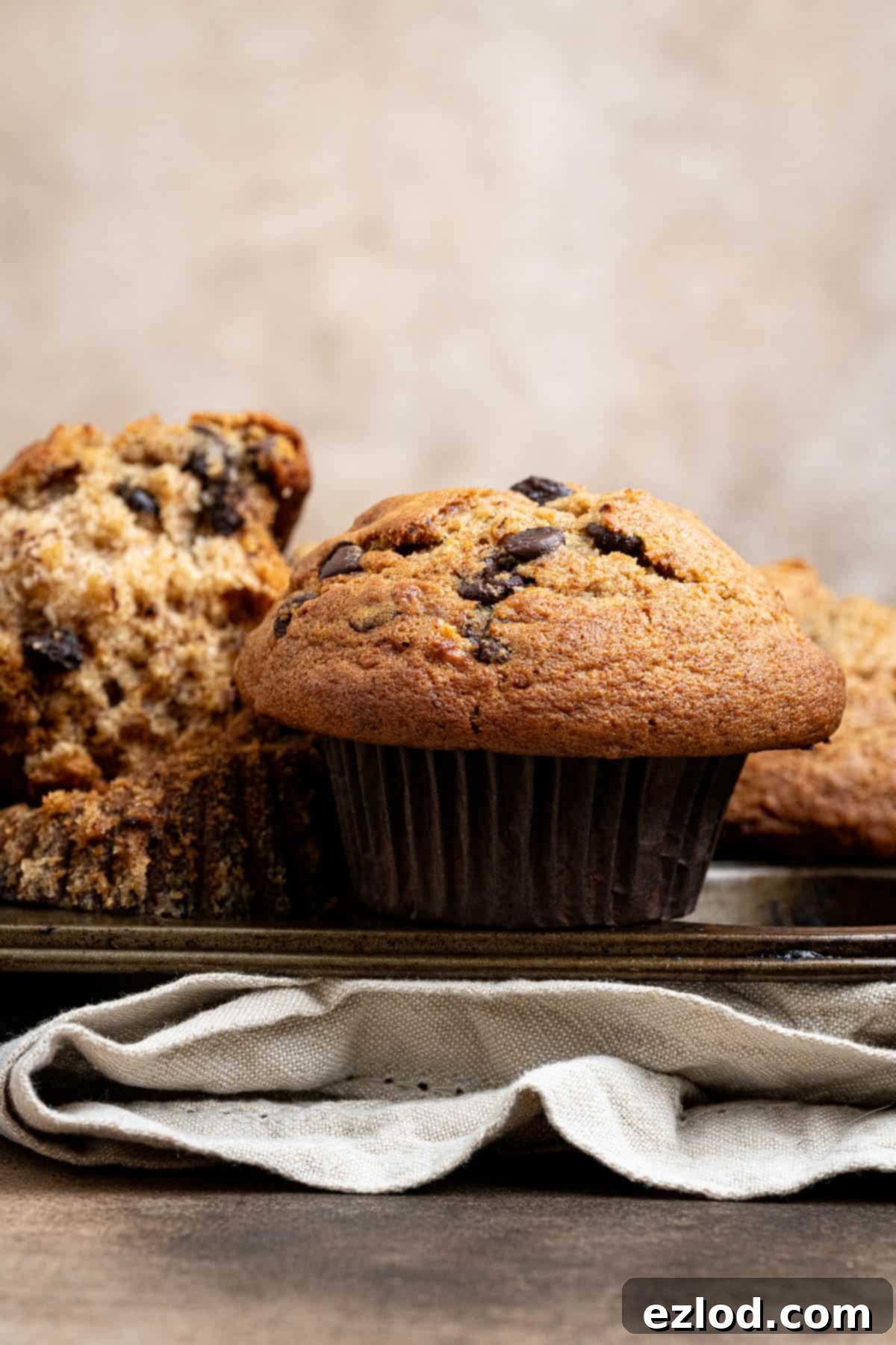 Close up of a single golden-brown vegan banana muffin, freshly baked with a tall domed top, resting on top of a muffin pan.