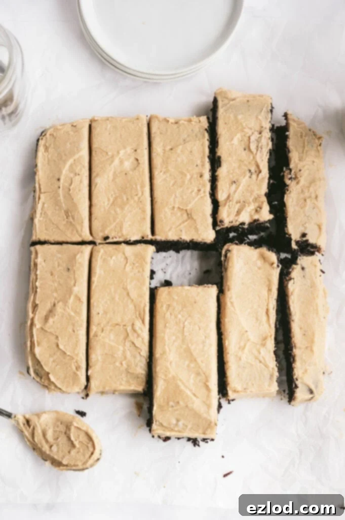 Overhead photo of Chocolate cake with peanut butter frosting cut into 10 rectangular pieces. There is a spoonful of frosting off to the side as well as round white plates. This image showcases the delicious presentation of a healthy, clean, gluten-free dessert ready to be enjoyed.