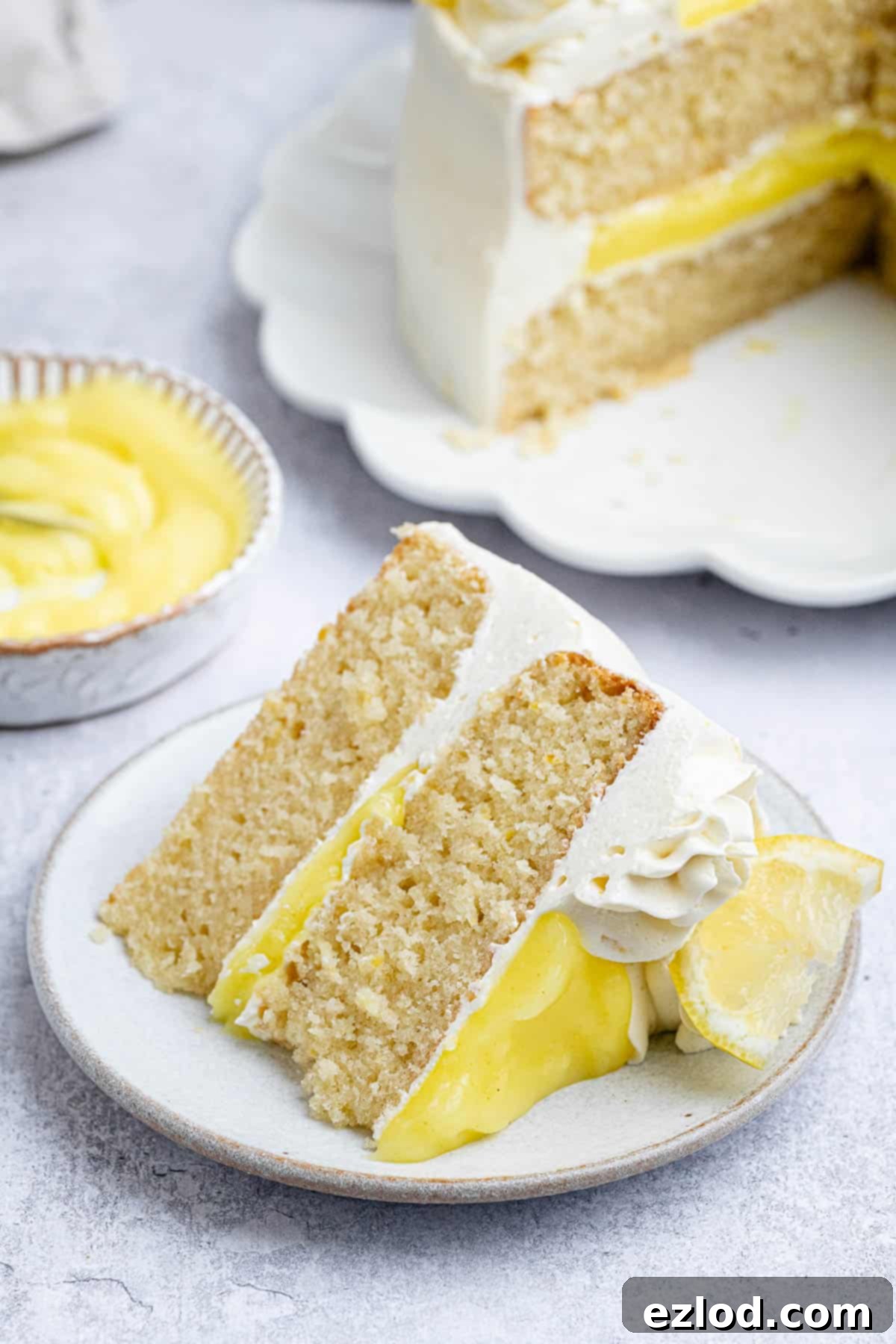 A beautifully presented slice of vegan lemon layer cake on a pristine white plate, showcasing its moist layers, creamy buttercream, and tangy lemon curd filling.