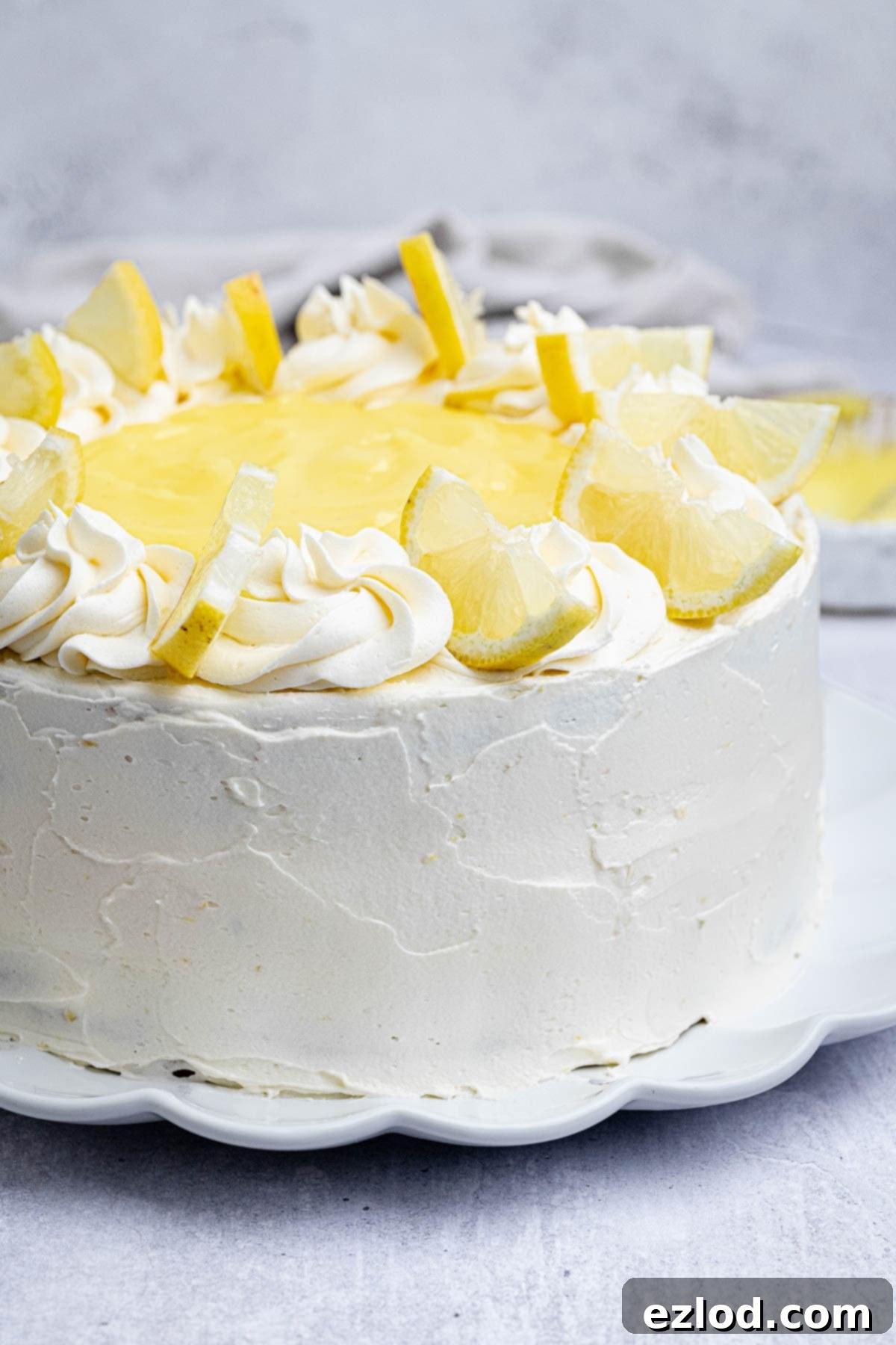 A fully assembled vegan lemon layer cake, beautifully topped with fresh lemon slices, resting on a clean white plate.