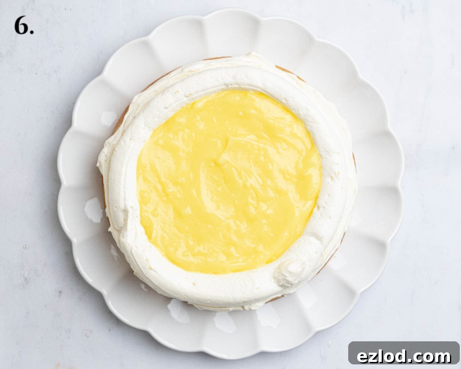 Step 6: The partially assembled vegan lemon layer cake, showing a piped buttercream border filled with tangy lemon curd, ready for the top layer.