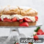 Vegan strawberry shortcake on a glass cake stand on a marble board.