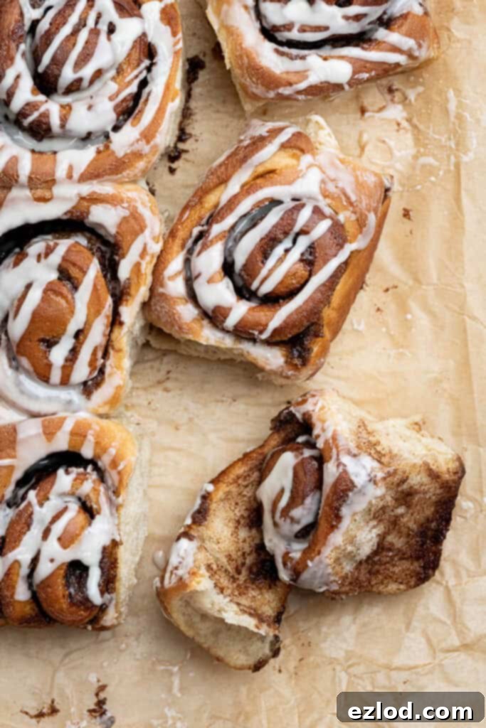 Vegan olive oil cinnamon  rolls on a sheet of brown baking paper, one of them unravelled.