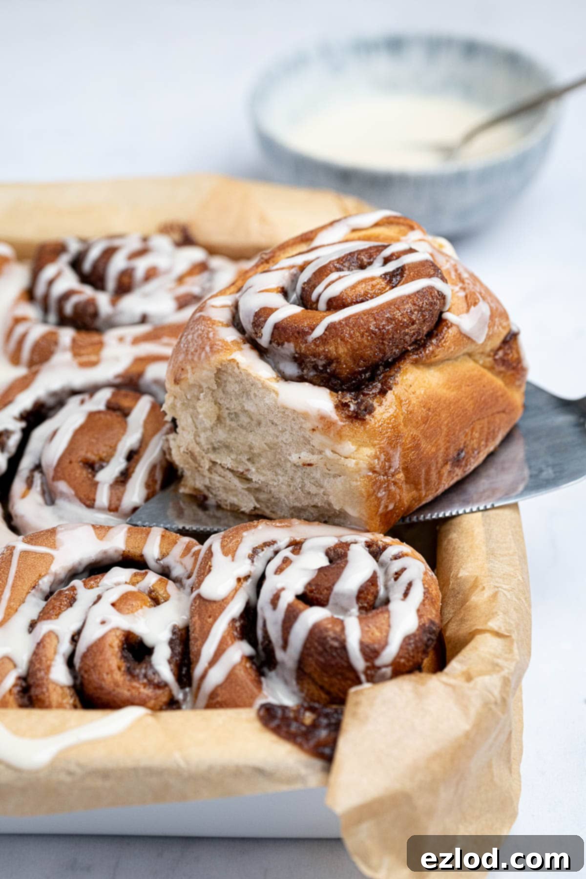 An olive oil cinnamon roll being lifted out of the tray on a cake slice.