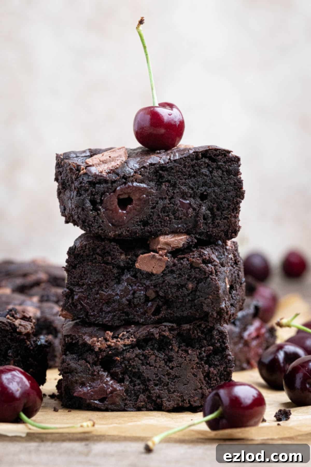 A stack of vegan black forest brownies with a cherry on top, highlighting the fudgy texture and juicy cherries.
