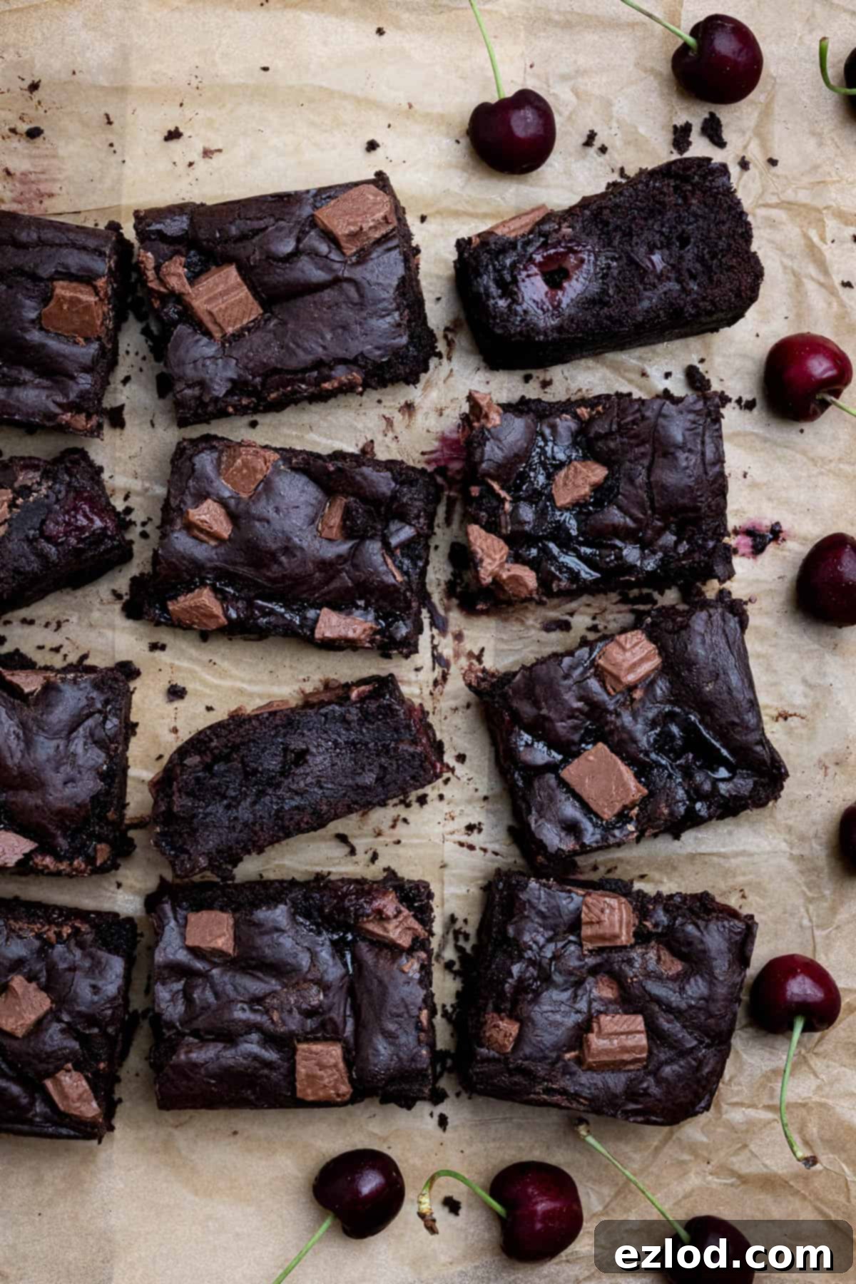 Vegan black forest brownies arranged on a sheet of brown baking paper with fresh cherries scattered around.