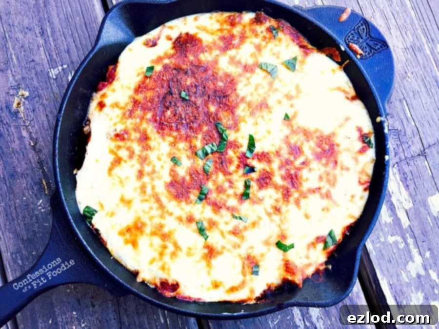 Overhead view of cast iron skillet filled with butternut squash lasagna. The top cheese layer has been broiled to a golden brown and garnished with basil.