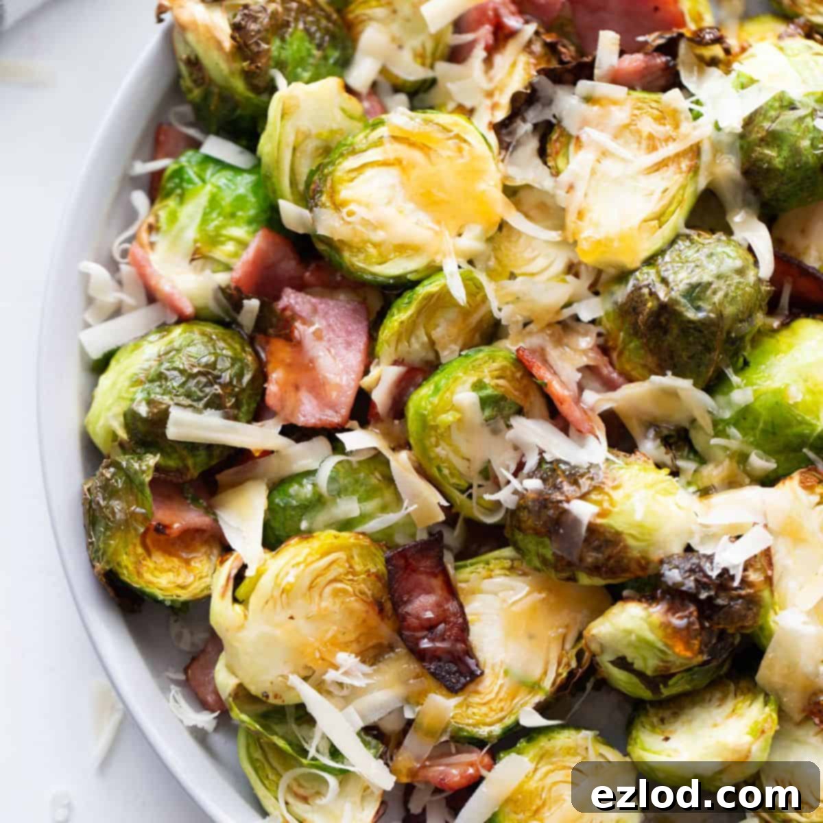 A vibrant plate of perfectly crispy Air Fryer Brussels Sprouts, garnished with crumbled bacon, shaved Parmesan, and a glistening drizzle of hot honey.