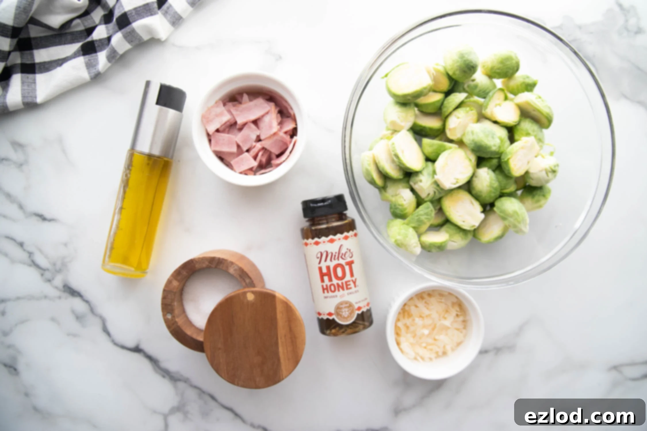 A flatlay of fresh Brussels sprouts, avocado oil spray, Pecorino Romano cheese, kosher salt, nitrate-free turkey bacon, and hot honey—all ingredients for Air Fryer Brussels Sprouts.