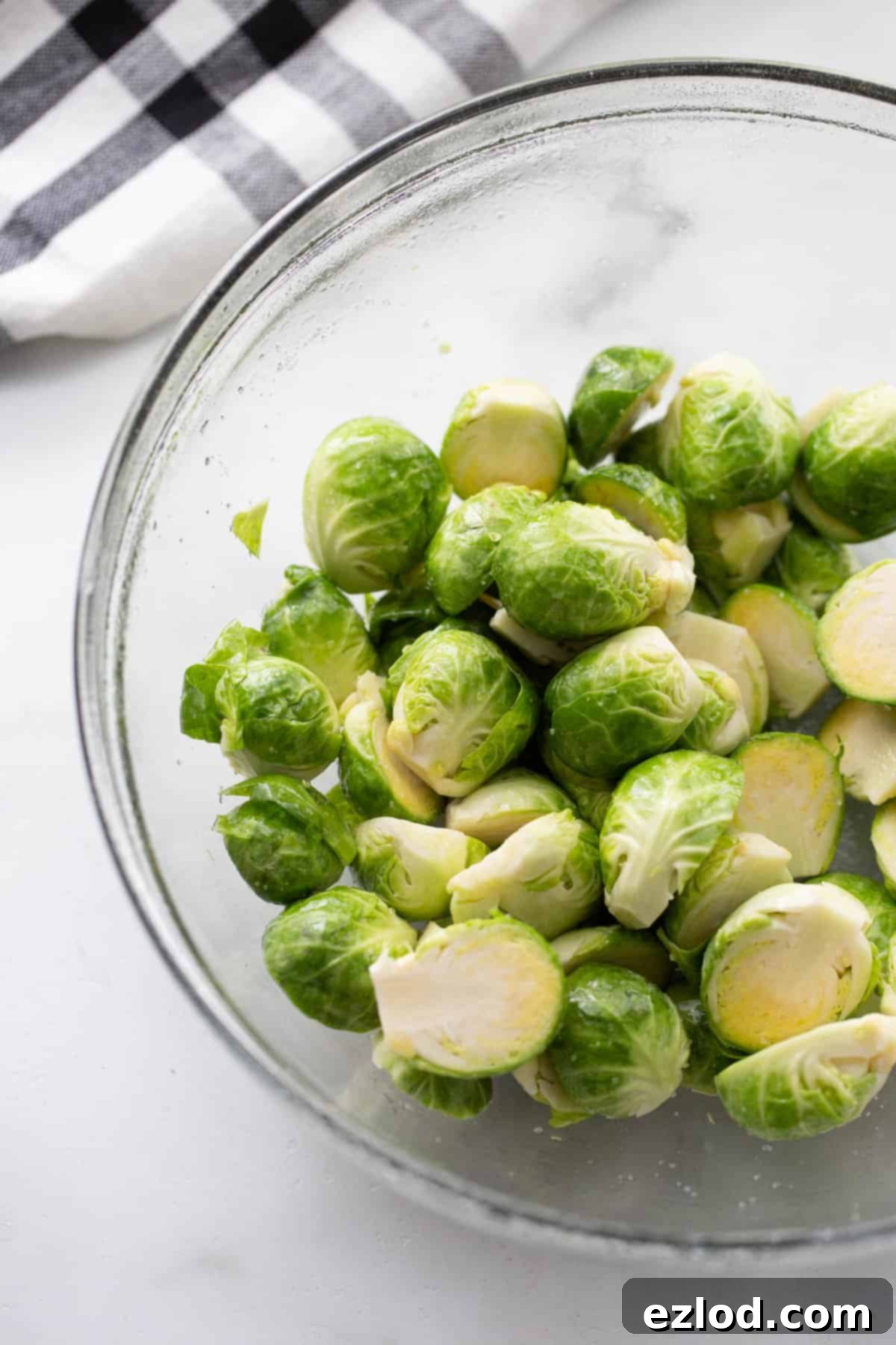 A bowl of fresh Brussels sprouts, halved and coated evenly with cooking oil and kosher salt, ready for the air fryer.