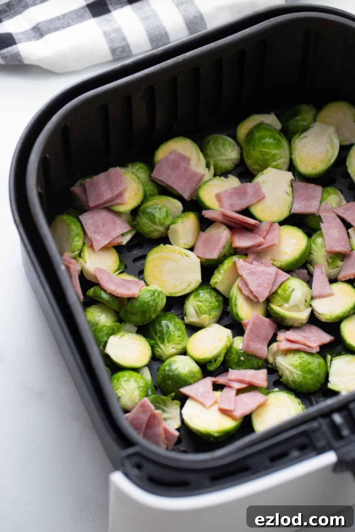 Halved Brussels sprouts and diced turkey bacon arranged in a single layer in an air fryer basket, ready for cooking.