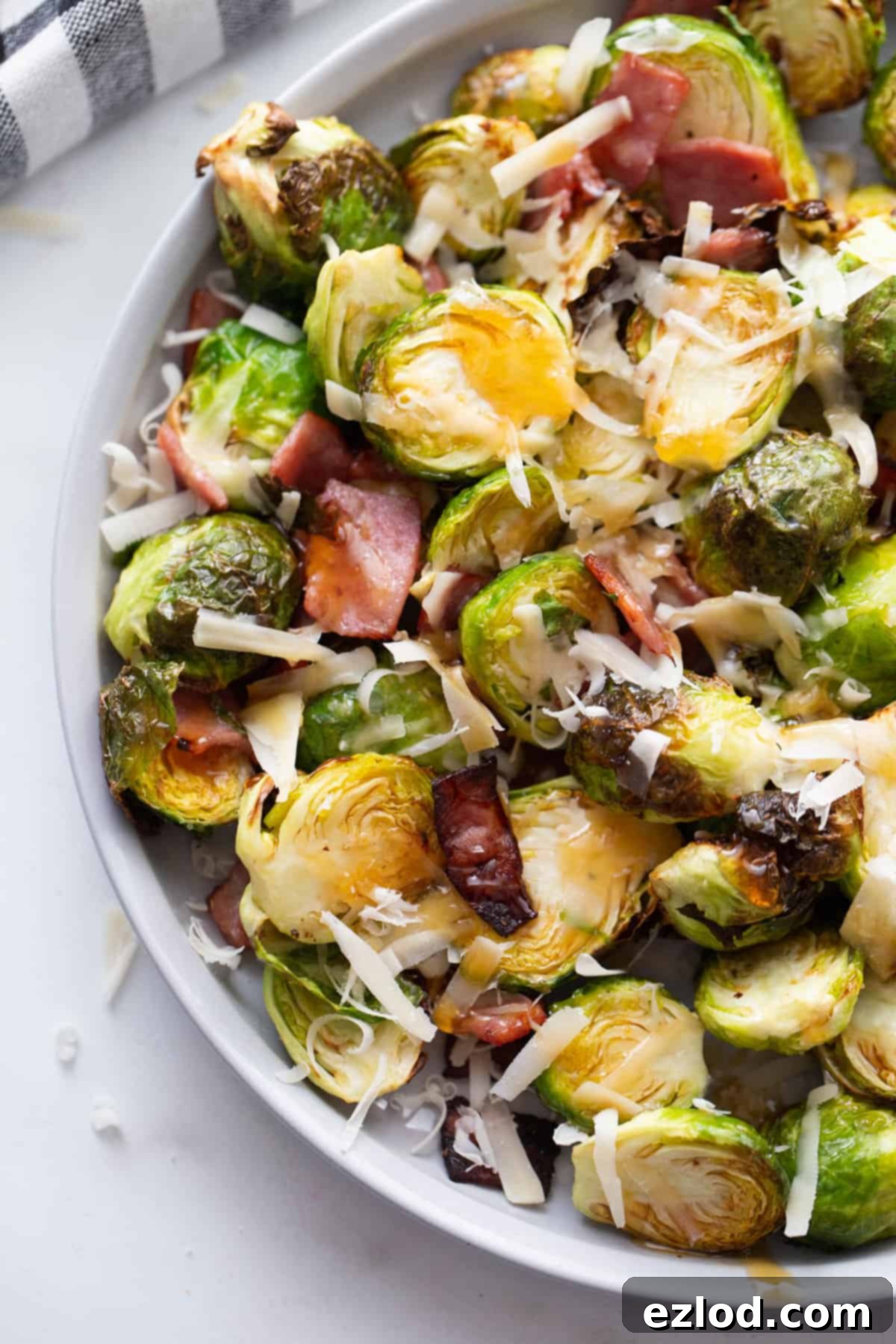 A beautifully plated serving of Air Fried Brussels Sprouts, generously topped with melted Parmesan cheese, crispy turkey bacon, and a final flourish of hot honey.