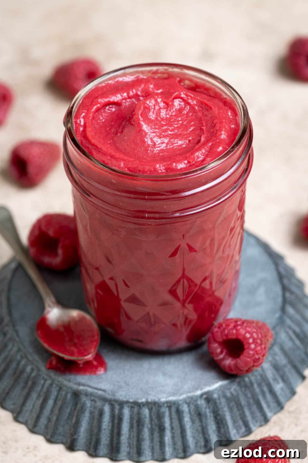 A close-up shot of a small glass jar filled with vibrant vegan raspberry curd, highlighting its smooth and creamy texture.