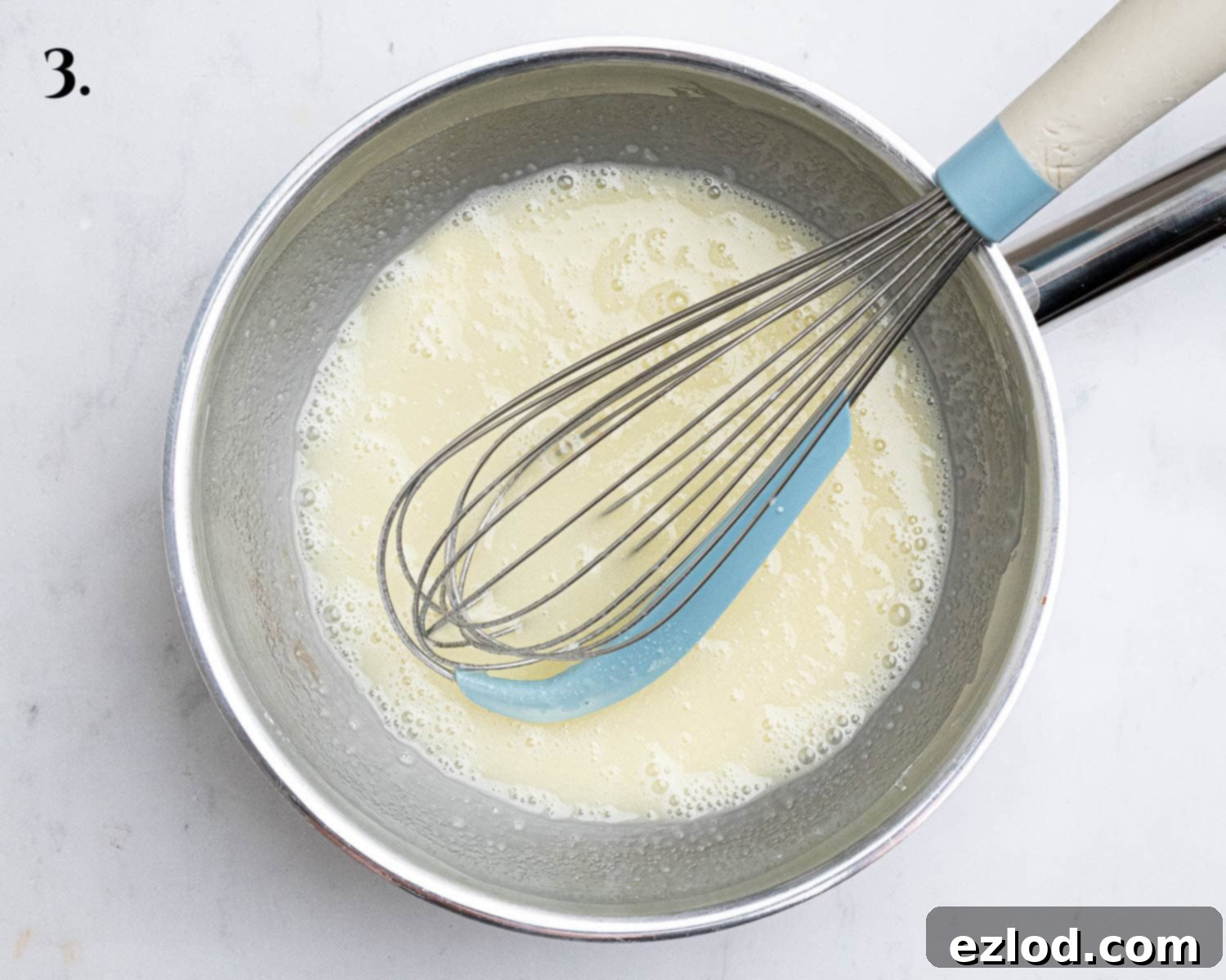 Step 3 in making vegan raspberry curd: A saucepan containing cornflour and non-dairy milk being whisked together, forming a smooth base.