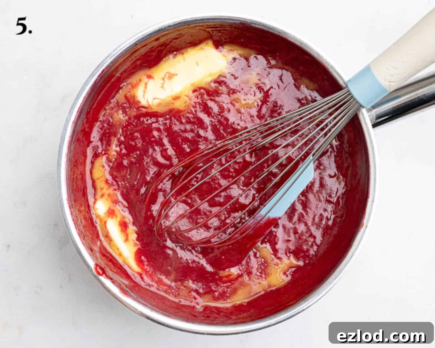 Step 5 in making vegan raspberry curd: Melted vegan butter being whisked into the warm, thickened raspberry curd for a smooth finish.