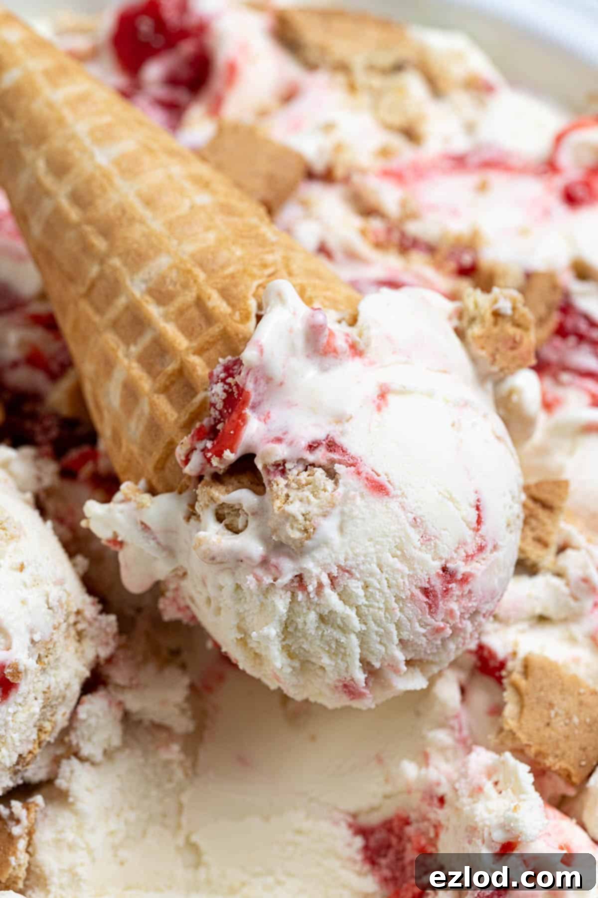 A close-up of a scoop of creamy vegan strawberry cheesecake ice cream, beautifully presented in a waffle cone.