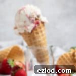 A scoop of homemade vegan strawberry cheesecake ice cream in a glass jar, surrounded by fresh strawberries and waffle cones.