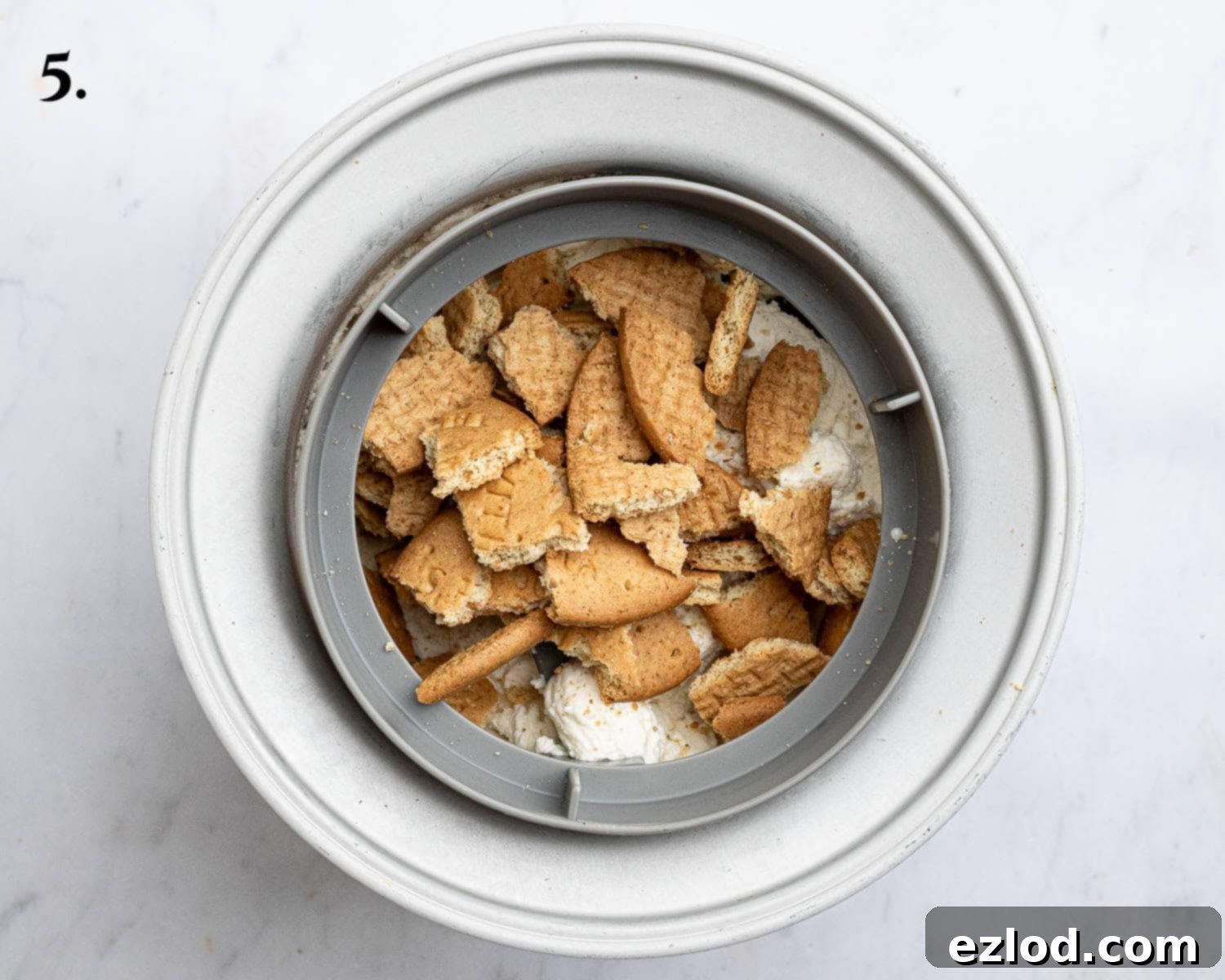 Step 5 in making vegan strawberry cheesecake ice cream: broken digestive biscuits being added to the churning ice cream in the ice cream maker.